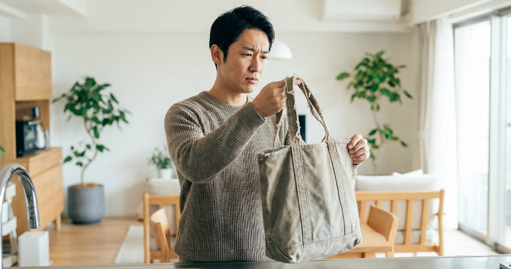 使い込んだトートバッグを見て買い替えを検討する日本人男性